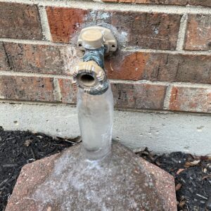 Frost-free outdoor spigot on a brick house encased in a thick layer of ice after freezing temperatures